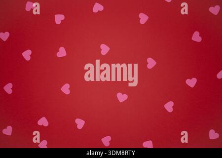 This image features a collection of delicate pink paper hearts scattered across a rich, textured red background. It's a perfect backdrop for Valentine Stock Photo