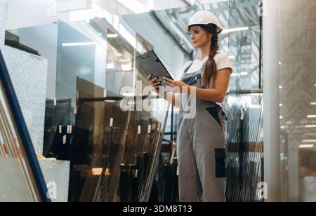 Reading the information, holding notepad. Woman is in the window making factory. Stock Photo