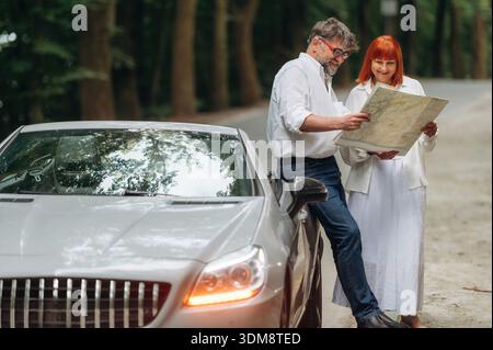 Reading the map. Lovely senior couple standing on the road near convertible cabriolet car. Stock Photo
