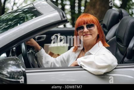 Having great time, in sunglasses. Side view of woman that is driving convertible cabriolet car. Stock Photo