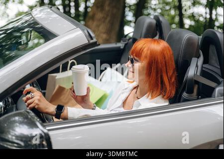 Having great time, in sunglasses. Side view of woman that is driving convertible cabriolet car. Stock Photo