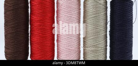 Spools of colored threads in a row close-up, are placed on a white surface. Equipment for tailoring and haberdashery. Stock Photo