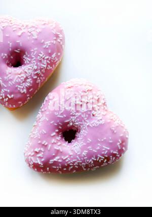 Two heart-shaped donuts with pink icing and sprinkles, isolated on a white background. Romantic or Valentine's Day theme. Overhead view. Stock Photo