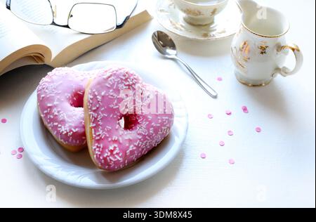 Two heart-shaped donuts with pink icing and sprinkles, served on a white plate. Romantic or Valentine's Day theme. Stock Photo