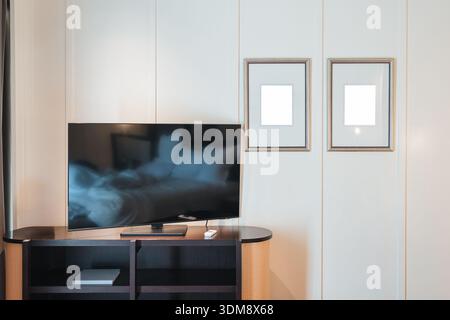 Contemporary hotel room interior featuring flat screen TV on wooden stand, White panel wall and two minimalist frame art wall Stock Photo