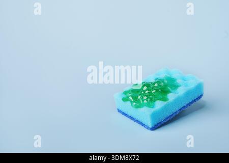 Blue cleaning sponge soaking green dishwashing liquid on blue background Stock Photo