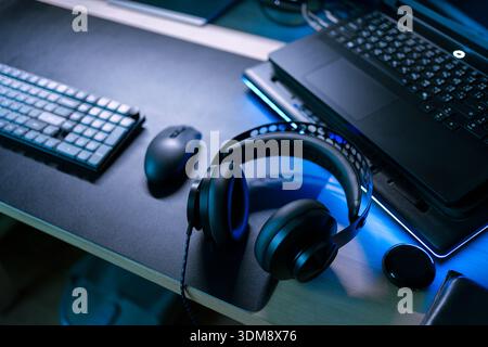 Modern gaming gear setup with laptop, wireless mouse, keyboard and headphone on desktop under cool blue light Stock Photo