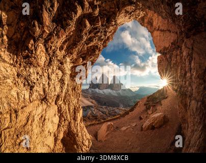 Grotta delle Tre Cime rocky tunnel framing sunset shines over Tre Cime di Lavaredo mountain peak in Dolomites, Italy Stock Photo
