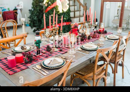 Elegant christmas dining table setup with red candles, seasonal ornamentals and classic tableware setting for holiday dinner home Stock Photo