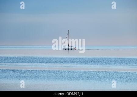 A lonely sailboat on the calm water of the Gulf of Trieste in Castelreggio under a hazy sky. Stock Photo
