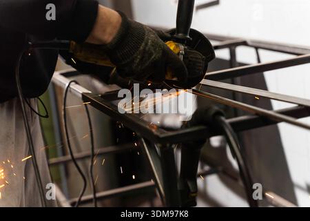Industrial worker uses angle grinder to cut metal with safety helmet on Stock Photo