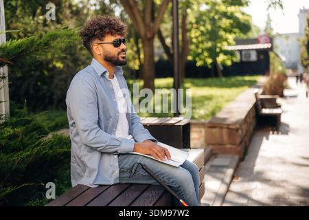 Sitting and reading using Braille. Blind man with white cane and sunglasses is in the city. Stock Photo