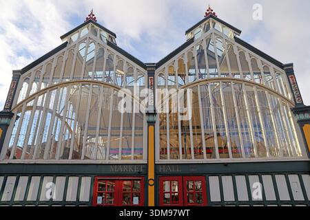 Upward view of the glass and timber sides of Stockport Market Hall in Market Place, showing the Victorian arched façade and red entrance doors Stock Photo