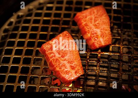 Marbled red beef steaks cooking on a traditional charcoal grill grate in a close-up shot. Stock Photo