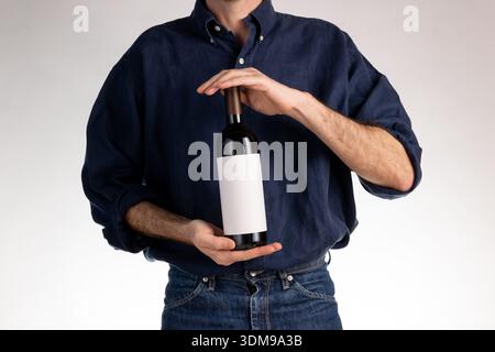 Guy in blue shirt and jeans with red wine bottle and premium paper label. Graphic label layout. online shop Stock Photo