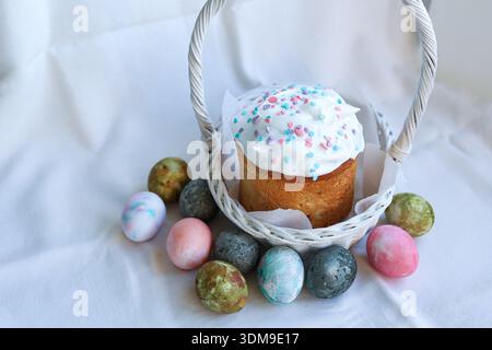 Orthodox Easter kulich placed in a white wicker basket with colorful painted eggs, traditional festive still life Stock Photo