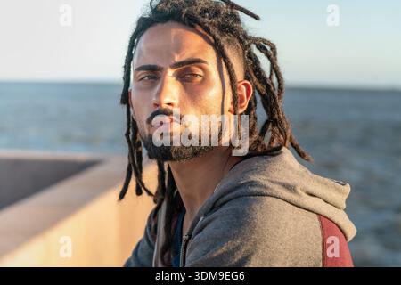 Young man with dreadlocks and beard standing outdoors by the sea Stock Photo