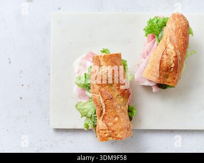 A lunch or breakfast table shows sliced sandwiches made with baguette, mozzarella cheese, ham, and lettuce. Fresh oranges and scrambled eggs are also Stock Photo