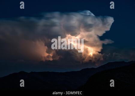 Thunderstorm with lightning inside a large cumulonimbus cloud over a mountain silhouette seen from Penser Joch Pass. Stock Photo