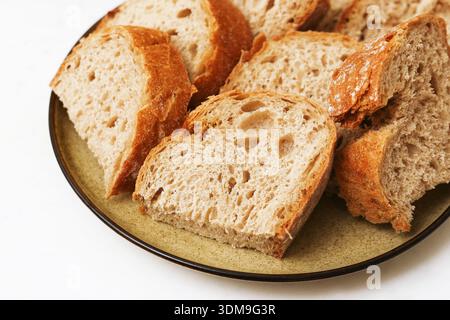 Sliced homemade bread on ceramic plate closeup. Fresh bakery product and traditional food concept with rustic loaf pieces for breakfast. Stock Photo