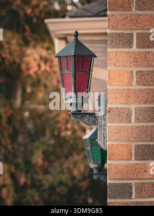 Decorative red and green lantern-style wall lights on a brick fire house exterior with autumn trees softly blurred in the background. Stock Photo