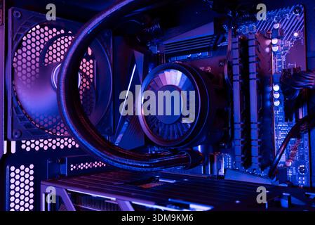 Interior of a modern desktop computer with liquid cooled processor, motherboard, cooling fan and internal components, illuminated with blue and purple Stock Photo