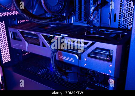Graphics card installed inside a modern desktop computer case with visible cooling system, power connectors and internal hardware under blue lighting Stock Photo
