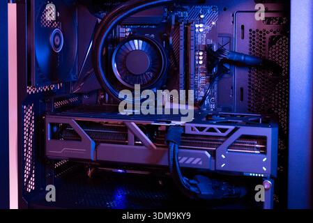 High performance desktop computer interior with graphics card, liquid cooling system, motherboard and power supply cables illuminated in dark modern l Stock Photo