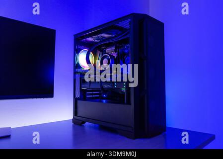 Gaming desktop computer with rgb cooling fan, liquid cooled processor and graphics card, positioned next to monitor in dark modern workspace Stock Photo