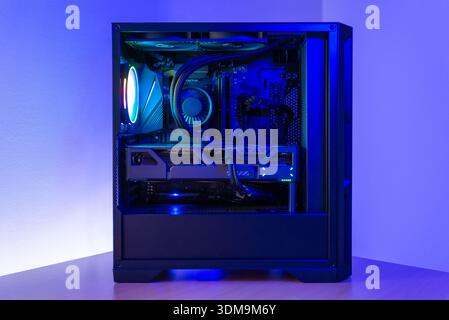 Modern gaming desktop computer with transparent case, liquid cooling, graphics card and rgb lighting, placed on desk in minimalist workspace environme Stock Photo