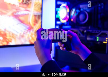 Hands holding game controller in front of gaming computer with rgb lighting and monitor, showcasing modern home gaming and entertainment setup Stock Photo