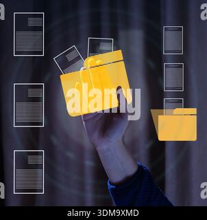 Human hand holding translucent yellow digital folder with documents on dark abstract background with file icons. File management concept, electronic a Stock Photo