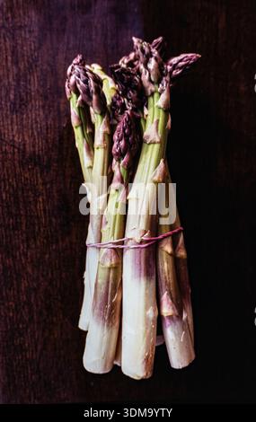Bundled green asparagus tied shown on dark wood textured surface. Top view, flat lay Stock Photo