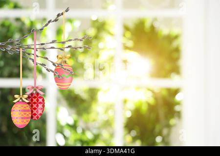 Easter eggs hanging from willow branches near window indoors Stock Photo