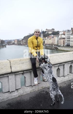 Luring and attracting a dog, dogownership, dog training, going walkies in city, person in a yellow jacket sits on a bridge as a dog jumps up to reach Stock Photo
