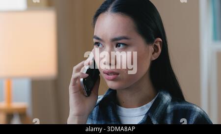 Angry Asian stressed woman arguing on mobile phone shouting upset at home call Korean Japanese Chinese girl female face yelling cellphone frustrated Stock Photo