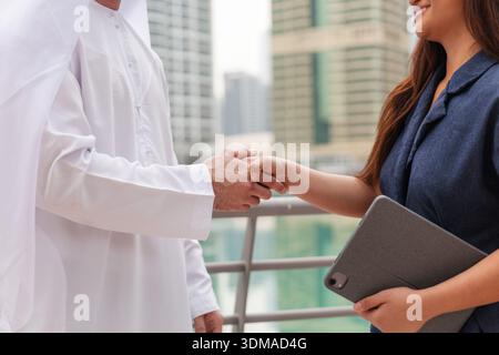 Business people, Arab man in traditional clothing, and an Asian entrepreneur woman shaking hands on a successful agreement. Stock Photo