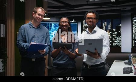 Portrait of smiling tech startup colleagues brainstorming ways to optimize performance in office. Happy programmers use devices for debugging, typing lines of code Stock Photo