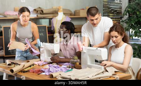 Young male teacher helping students sew while other drawing paper Stock Photo