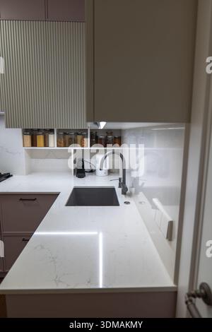 Compact kitchen corner shows white marble look countertop, square undermount sink, matte gray gooseneck faucet, labeled spice jars, espresso machine, Stock Photo