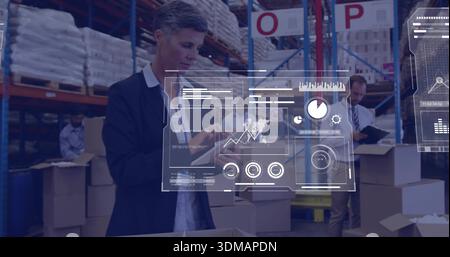 Supervising logistics supervisor wearing blazer tapping tablet in warehouse, with HUD and boxes Stock Photo