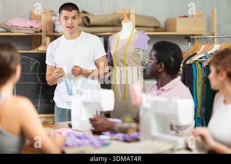 Young sewing instructor guiding adult beginners during practical workshop Stock Photo