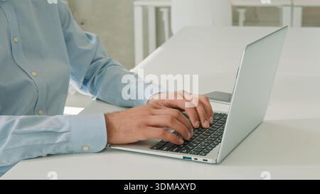 Cheerful happy Indian Arabian business man millennial entrepreneur working online on laptop inside office typing email chatting client smile male Stock Photo