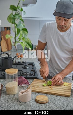 Man is slicing fresh lime on a wooden cutting board in a modern kitchen Stock Photo