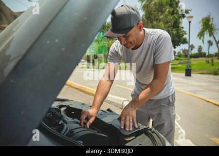 Man troubleshooting a broken down car by checking its engine on the side of the road Stock Photo