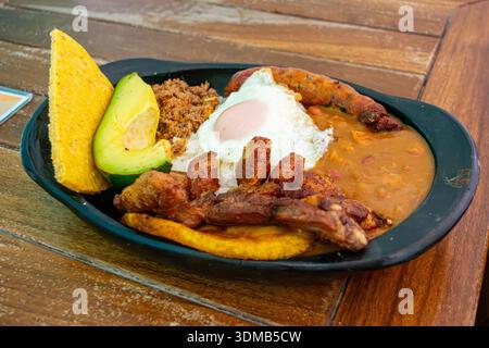 A vibrant bandeja paisa featuring an egg, avocado, and plantains served on a black plate. Stock Photo