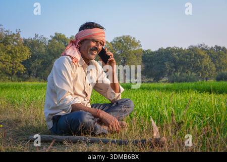 Indian farmer talking on mobile phone in green field. Digital connectivity in rural farming life Stock Photo