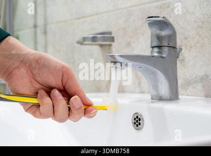 Rinsing toothbrush under running water in bathroom sink, daily oral hygiene concept Stock Photo