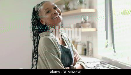 Smiling woman wearing striped apron leaning by gas stove near large window, with shelves and watch Stock Photo