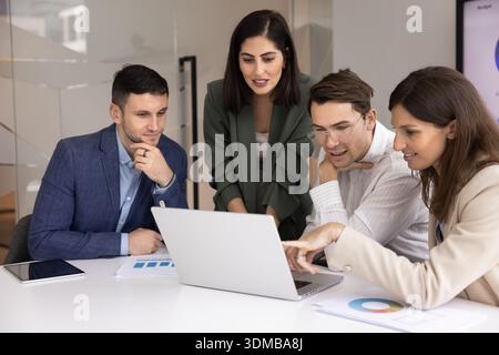 Four professionals collaborating around laptop in modern conference room Stock Photo